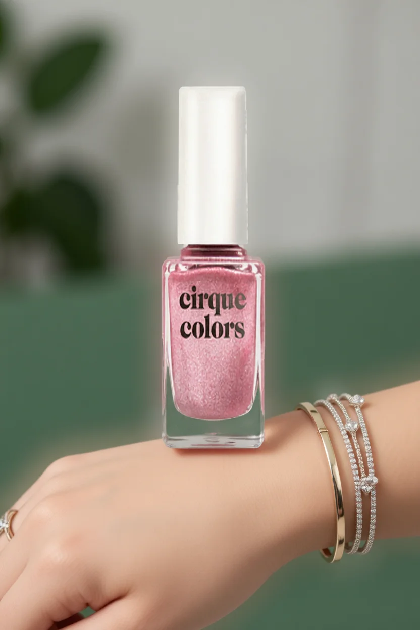 Frasco de esmalte rosa glitter Cirque Colors sobre mano con brazaletes