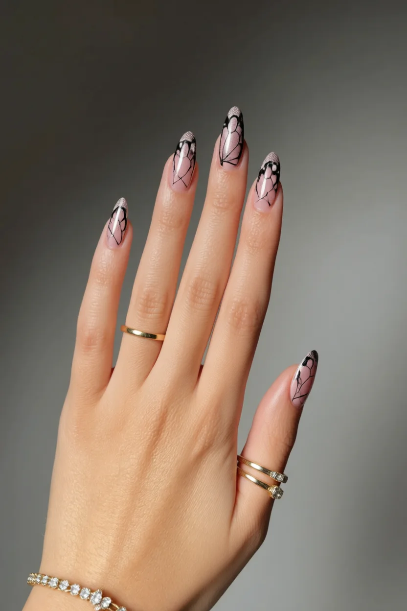 Mano con uñas almendradas largos con diseño abstracto negro sobre base nude y anillos dorados