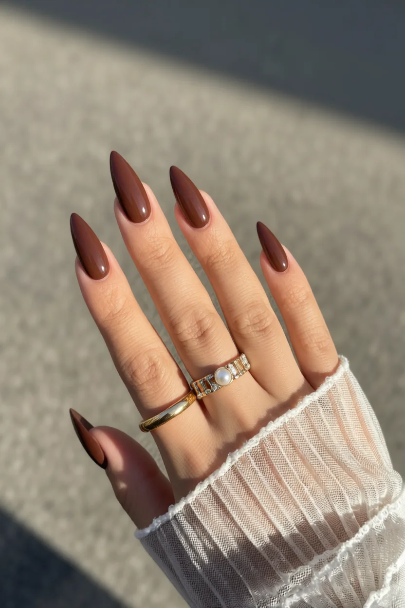 Mano con uñas largas color chocolate brillante y anillos