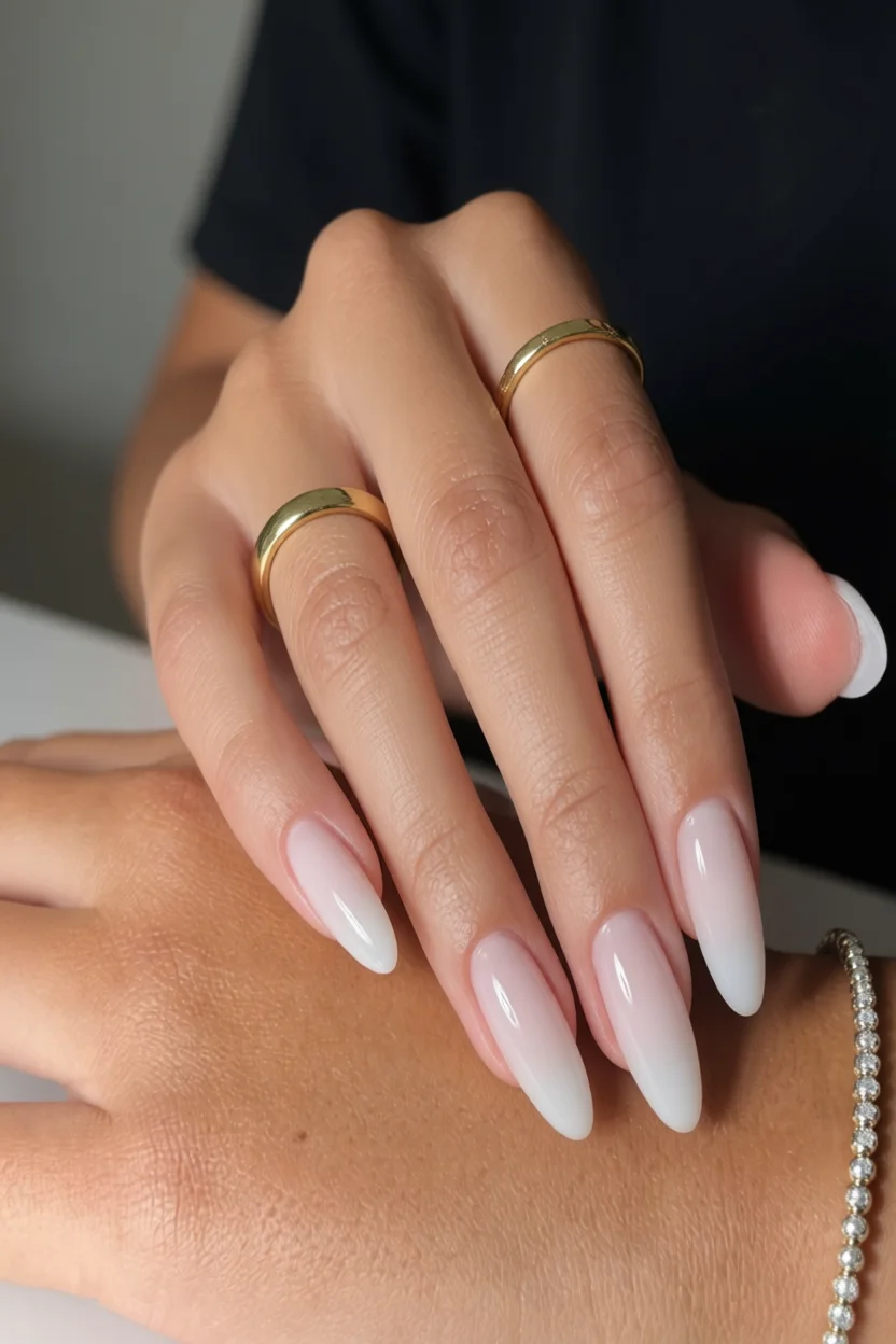 Mano con uñas almond degradadas de nude a blanco con anillos dorados