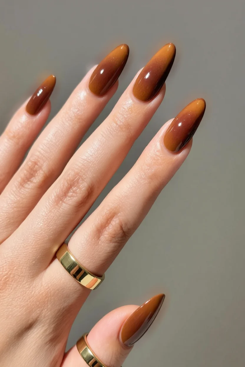 Mano con uñas largas en forma de almendra y degradado en tonos chocolate desde miel hasta marrón oscuro