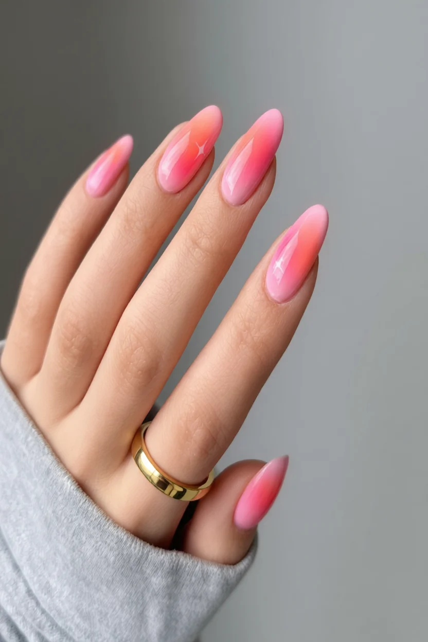 Mano con uñas largas ovaladas y diseño ombré en degradado rosa con brillo glossy y anillo dorado