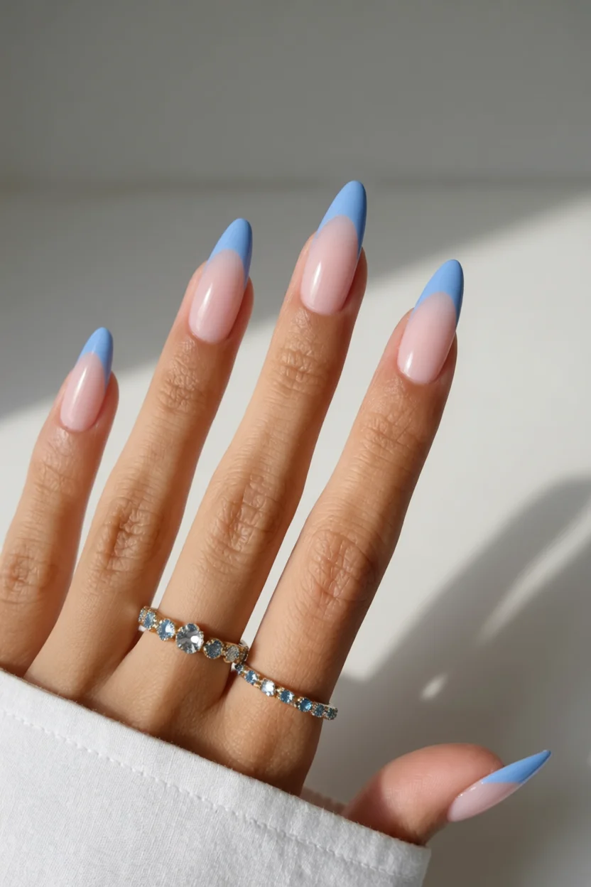 Mano con uñas largas en forma de almendra con diseño francés en azul cielo sobre base rosada nude