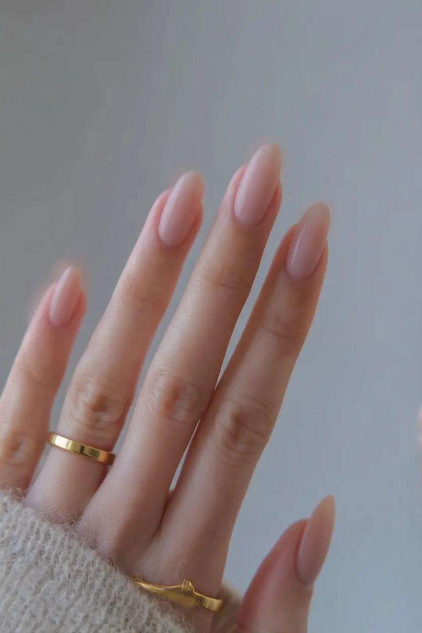 Mano con uñas largas almendradas en rosa nude brillante y anillos dorados