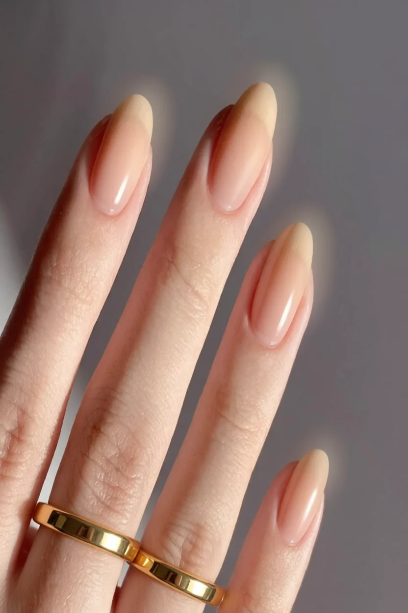Mano con uñas largas almendradas nude brillante y anillos dorados