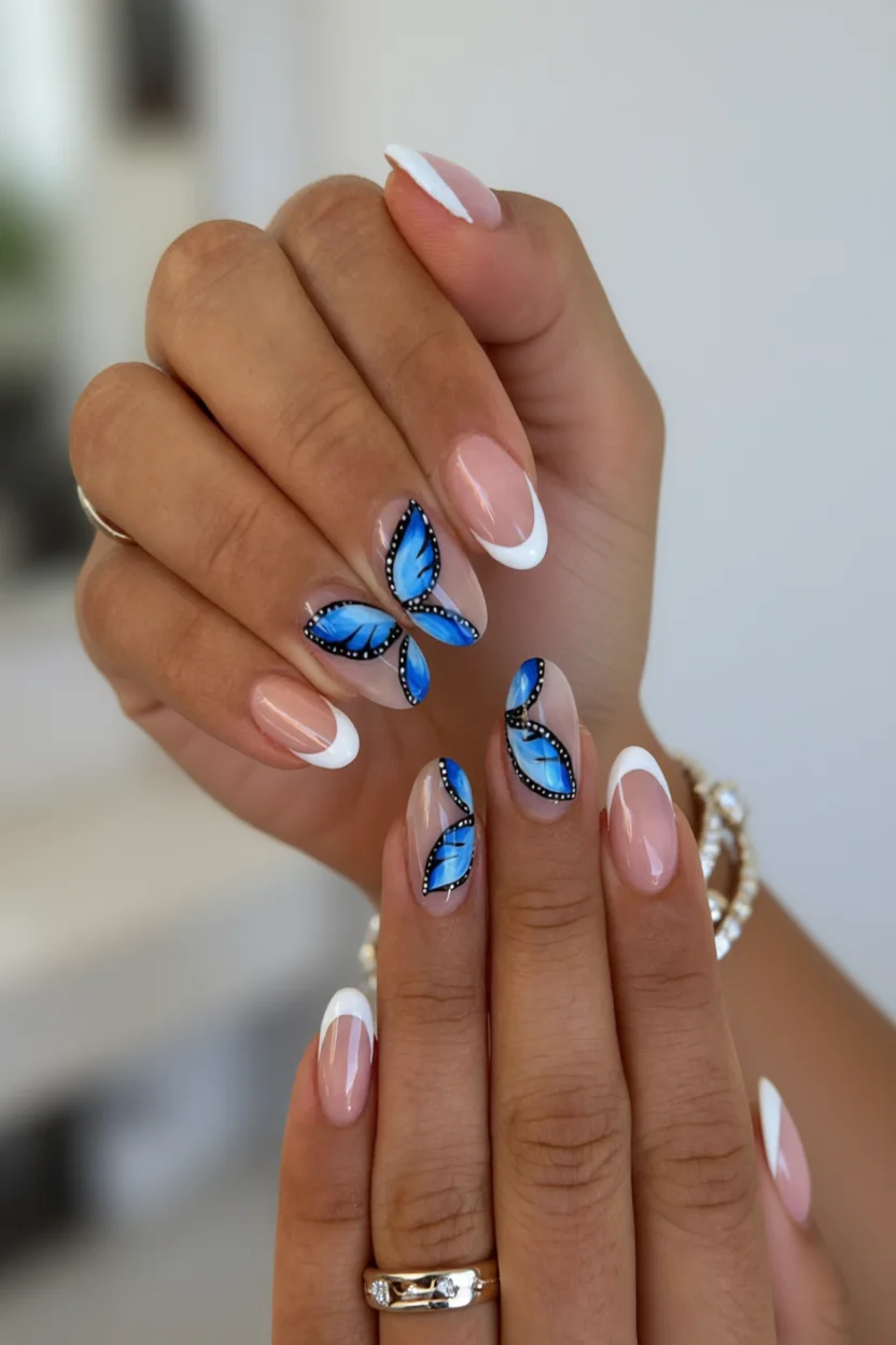 Mano con uñas francesas nude y decoración de alas de mariposa azul
