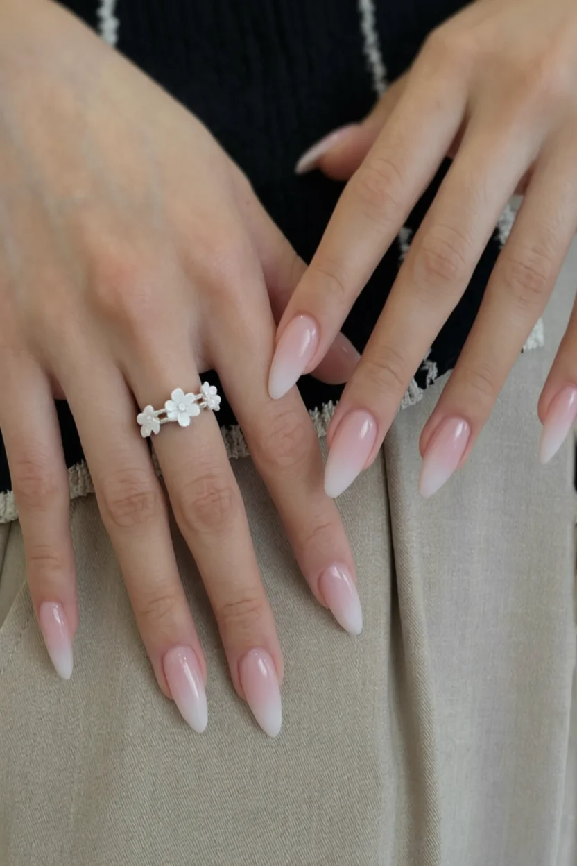 Uñas largas en forma de almendra con degradado ombré rosa pálido a blanco y anillo de flores blancas