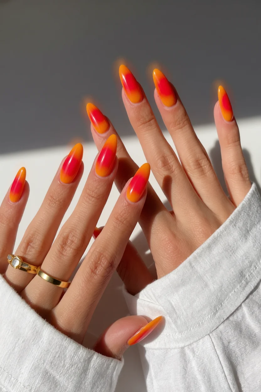 Mano con uñas largas en forma de almendra y degradado naranja a rosa