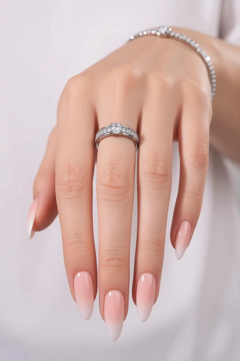 Mano con uñas largas forma almendra en degradado rosa a blanco, anillo de diamantes y pulsera
