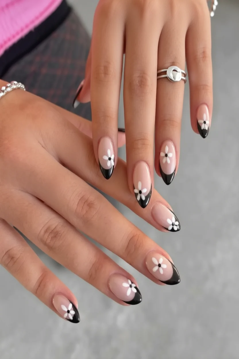 Mano con uñas estilo almendra, punta negra francesa y delicadas flores blancas pintadas a mano