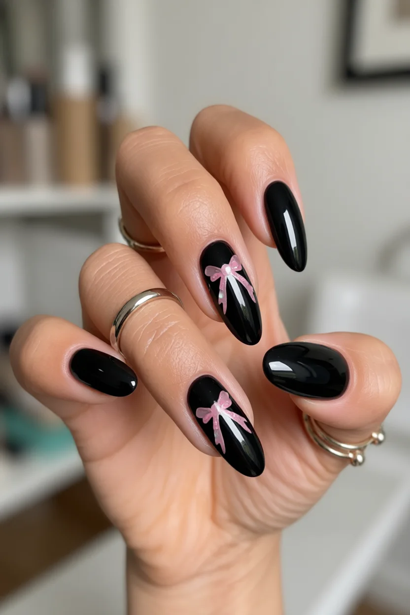 Uñas negras ovaladas con lazos y brillantes rosados