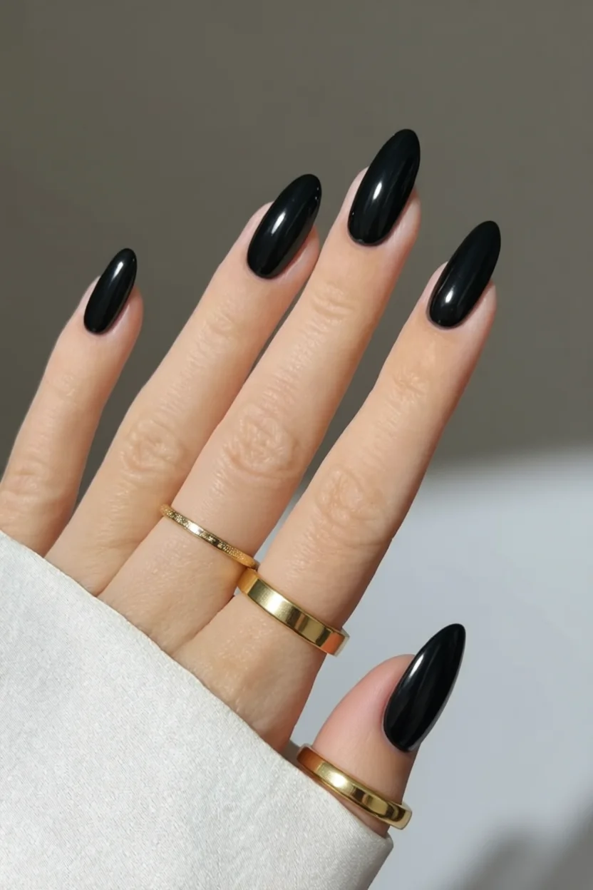 Mano con uñas largas forma almendrada pintadas de negro brillante con anillos dorados