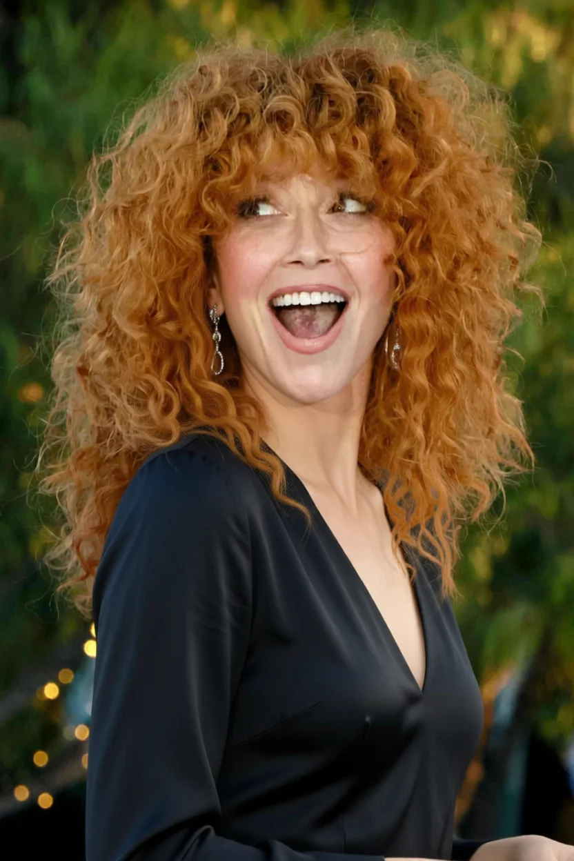 Mujer sonriendo con cabello rizado rojizo voluminoso y vestido oscuro