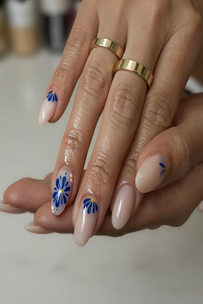 Manicura almendrada con base nude y motivos florales azules con centro amarillo