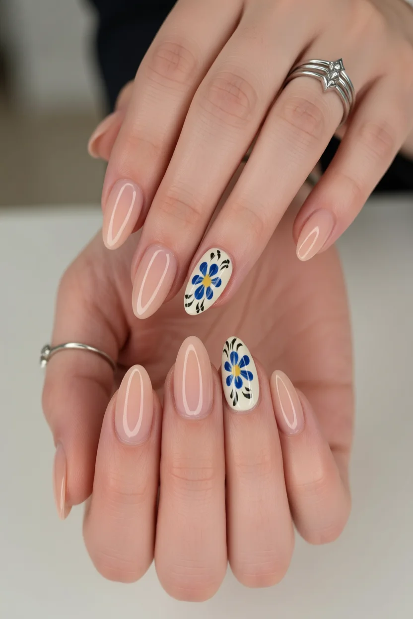 Uñas almendradas con base nude, puntas francesas blancas y acentos de flores azules en anulares