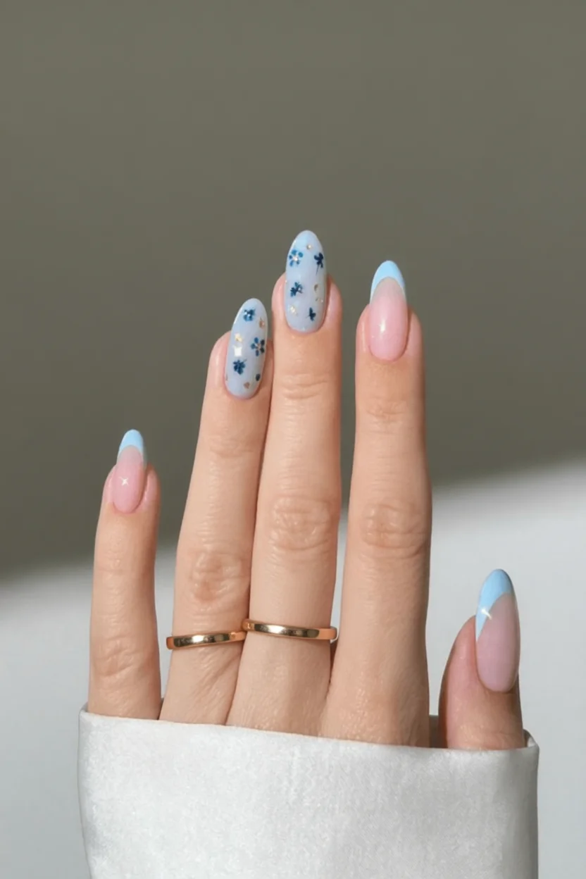 Mano con uñas largas almendradas con diseño floral azul y tips pastel