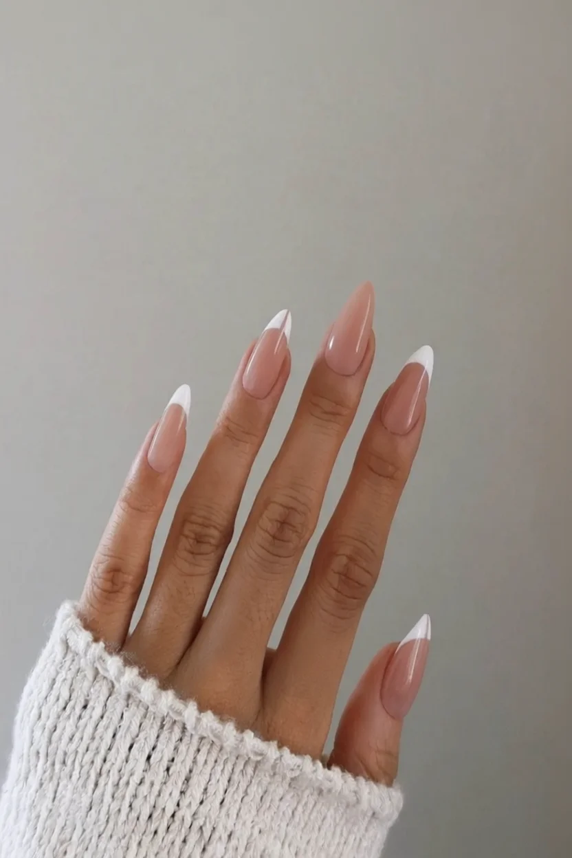Mano con uñas stiletto en french tip nude con puntas blancas brillantes