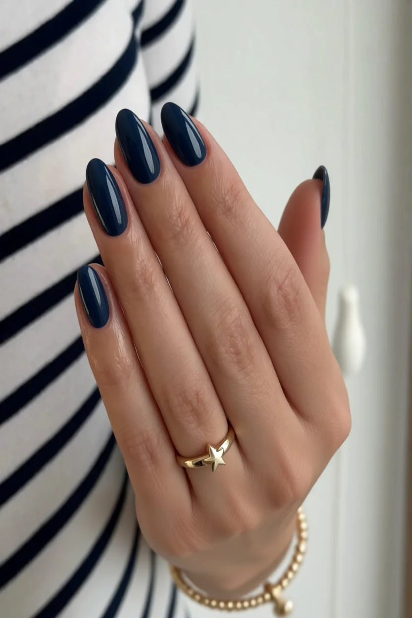 Mano con uñas ovaladas pintadas en azul marino brillante y anillo dorado de estrella