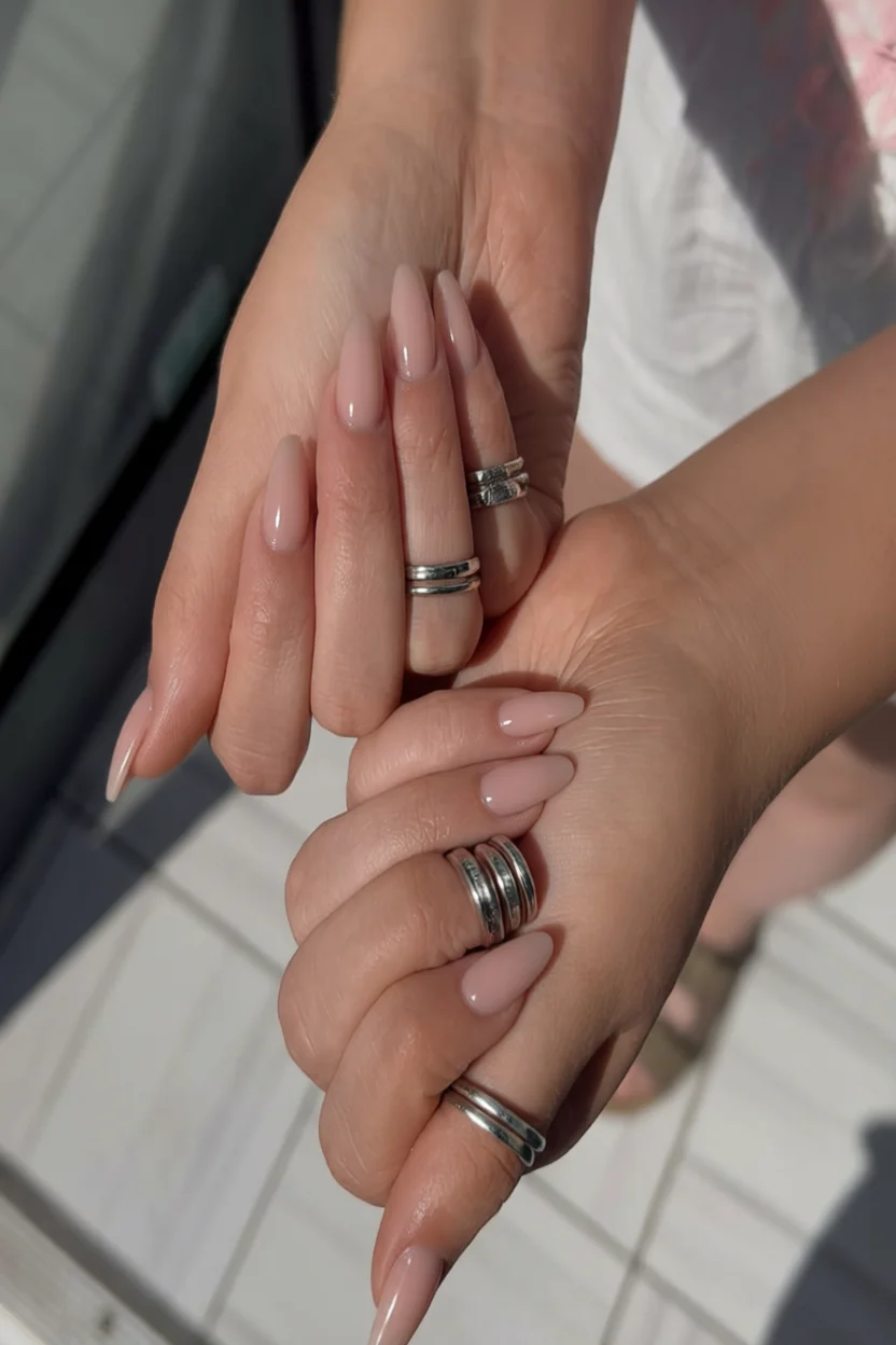 Manos con uñas largas en forma de almendra color nude brillante y anillos plateados apilados