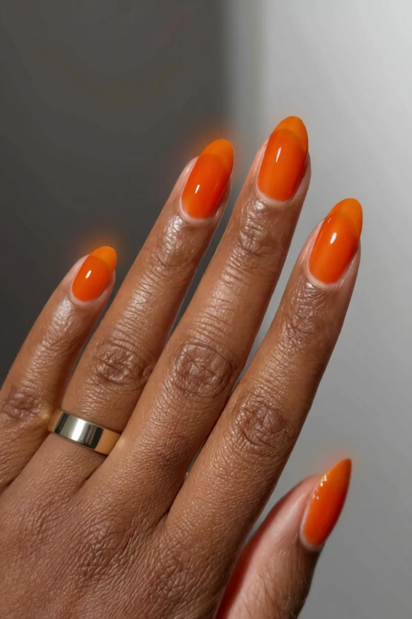 Mano con uñas en forma almendrada pintadas de naranja brillante con efecto degradado y acabado gloss