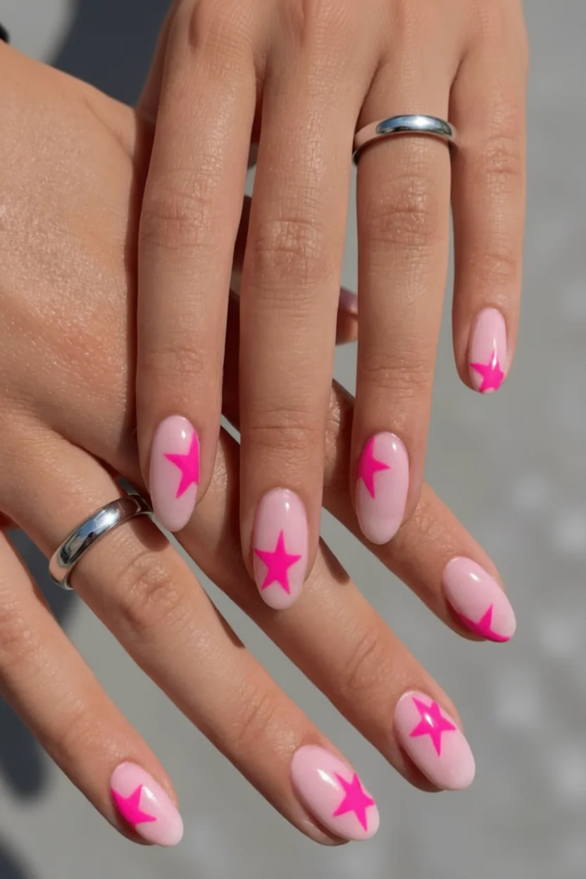 Mano con uñas ovaladas efecto lechoso rosa y estrellas fucsias decorativas