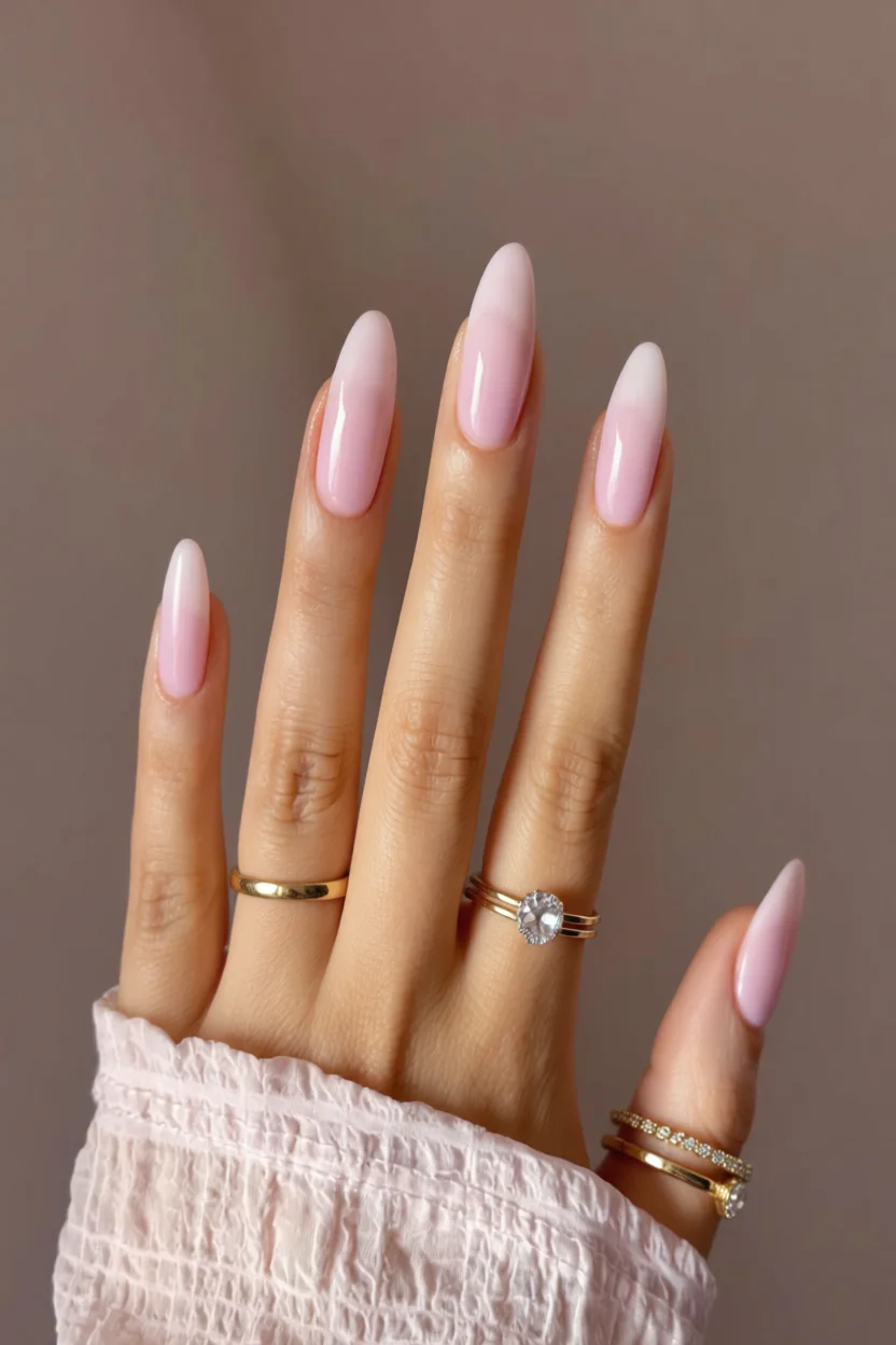 Mano con uñas largas forma almendra en efecto milky rosa degradado y brillo glossy