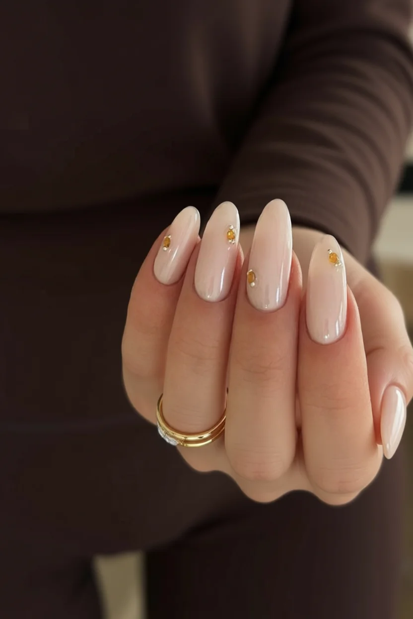 Uñas largas almendradas en tono nude con pequeños cristales dorados