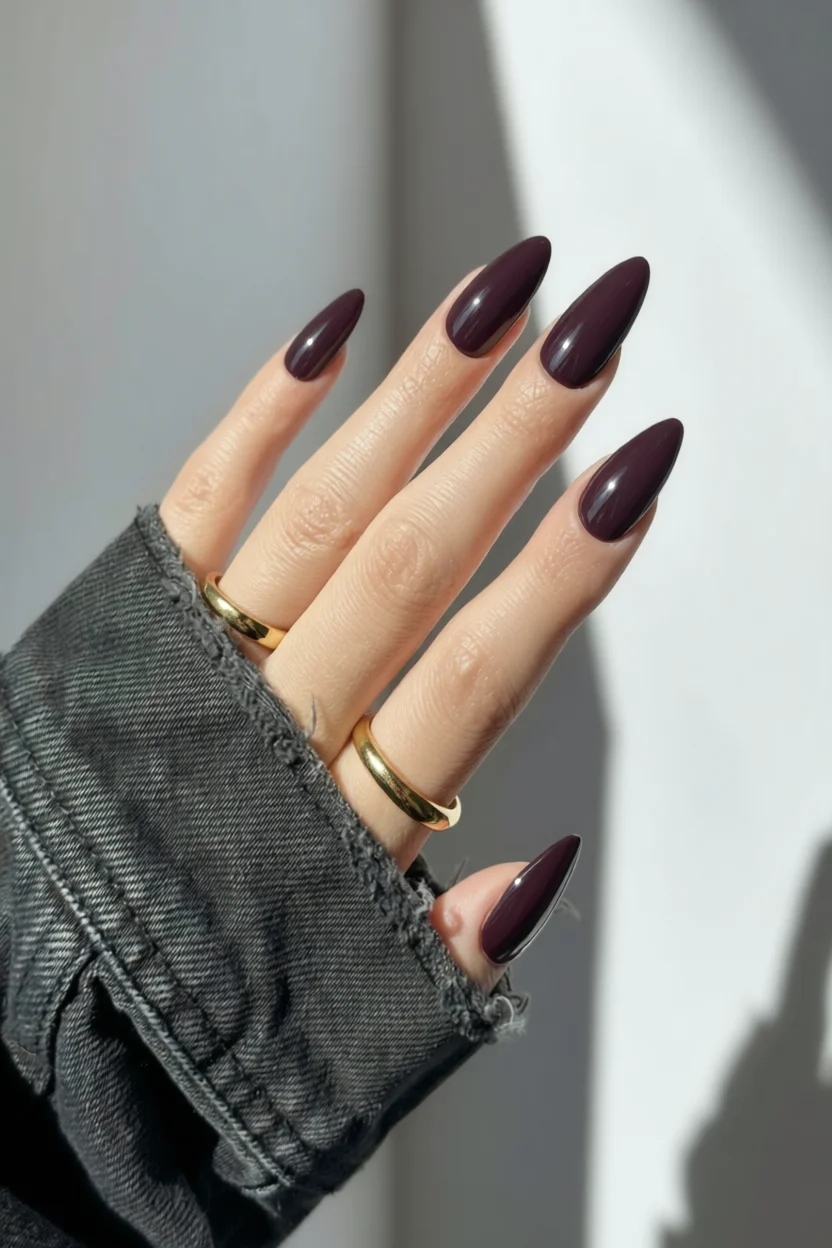Uñas almendradas largas en esmalte color vino con acabado brillante y anillos dorados