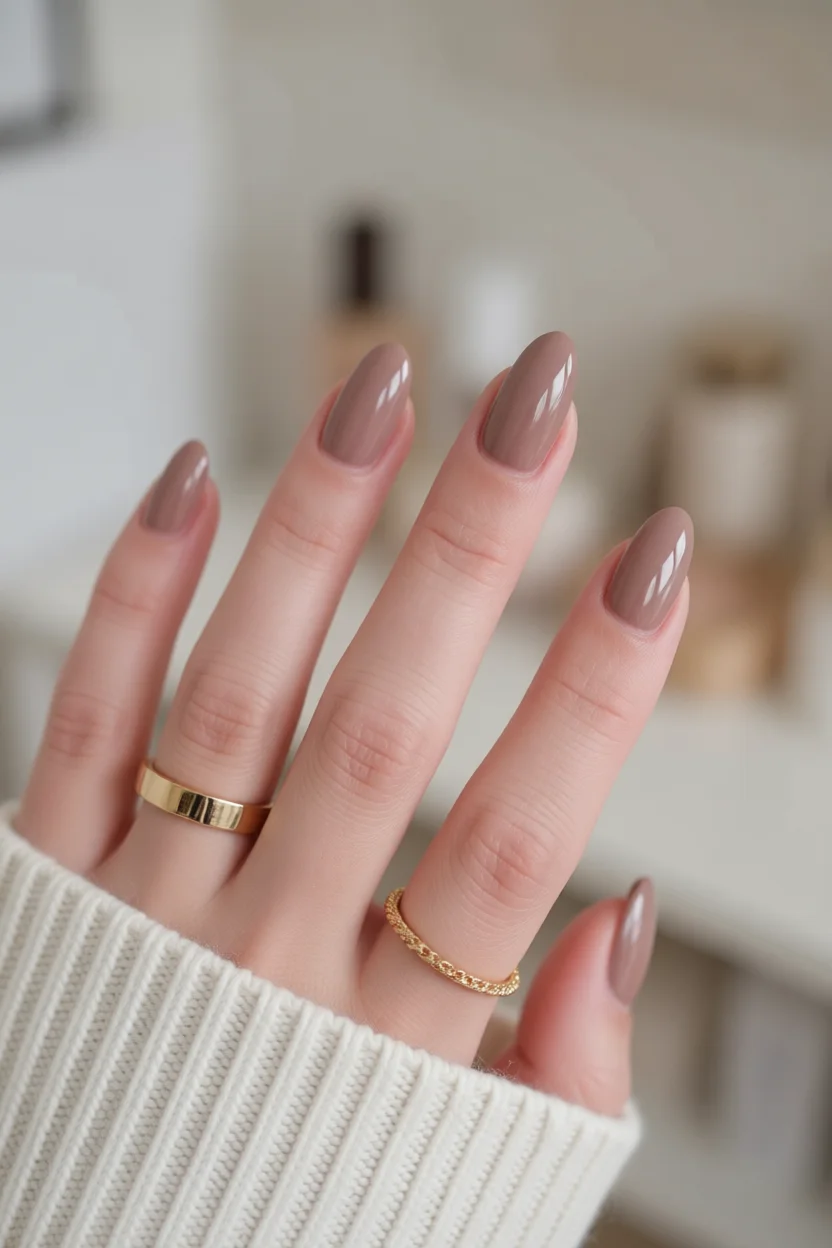 Mano con uñas marrones sólidas en forma de almendra y brillo intenso