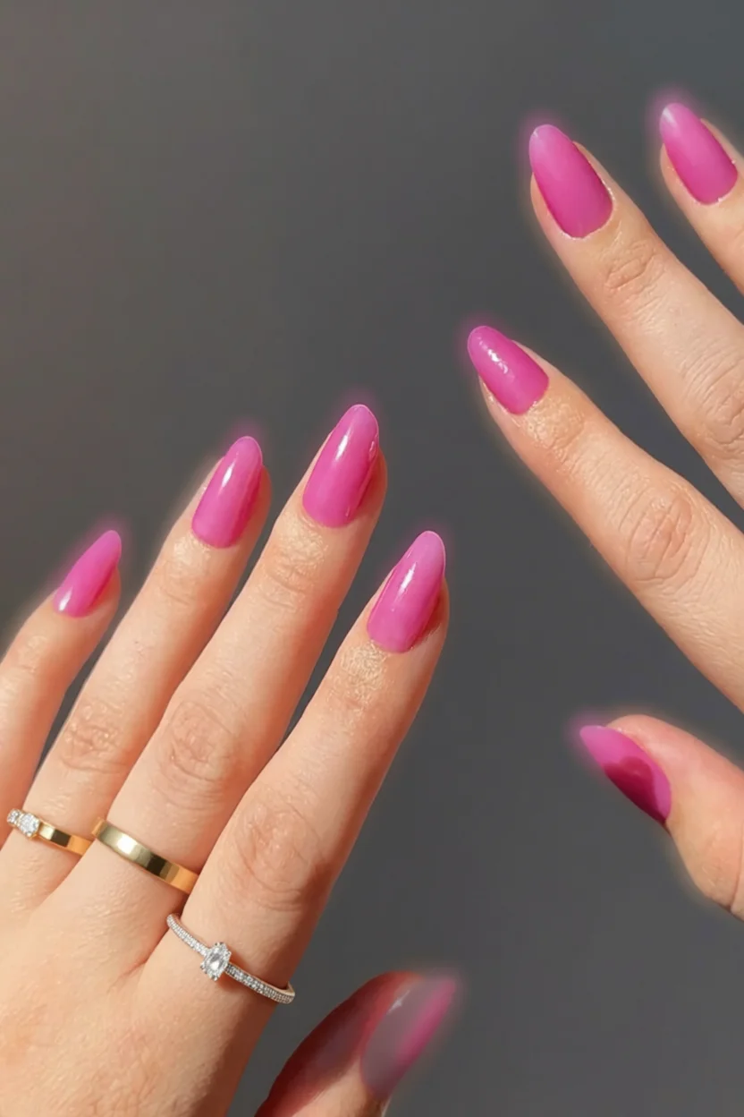 Mano con uñas ovaladas pintadas de rosa vibrante brillante