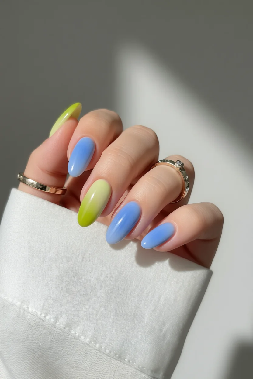 Manicura con uñas ovaladas degradadas de verde lima a azul cielo y acabado brillante