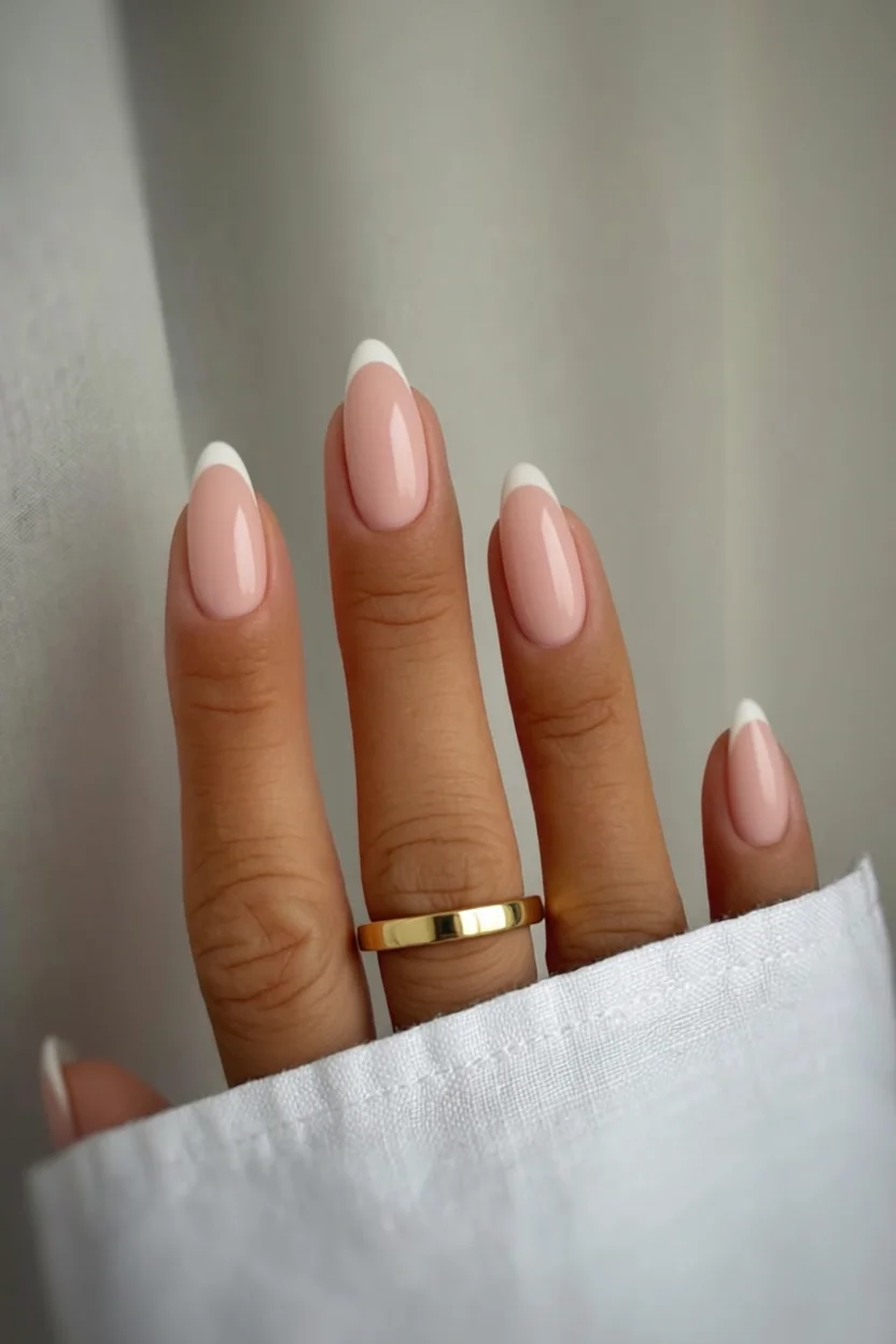 Mano con uñas ovaladas en diseño francés rosado con puntas blancas y anillo dorado