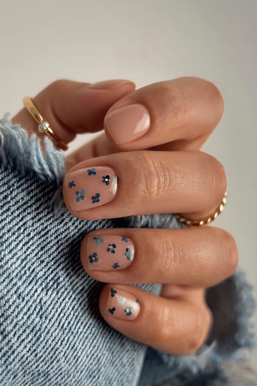 Uñas cortas con flores azules y brillo sobre base nude