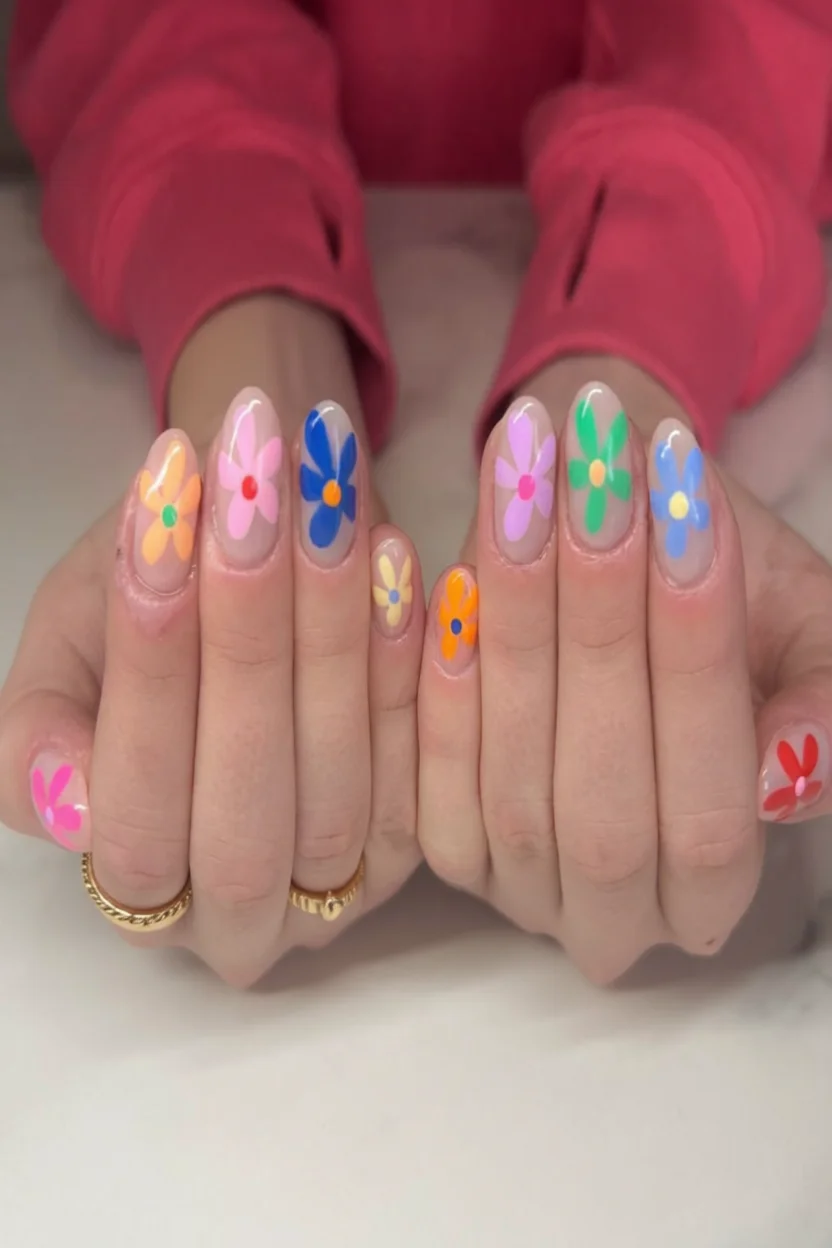 Manos con uñas ovaladas decoradas con flores multicolor sobre base nude