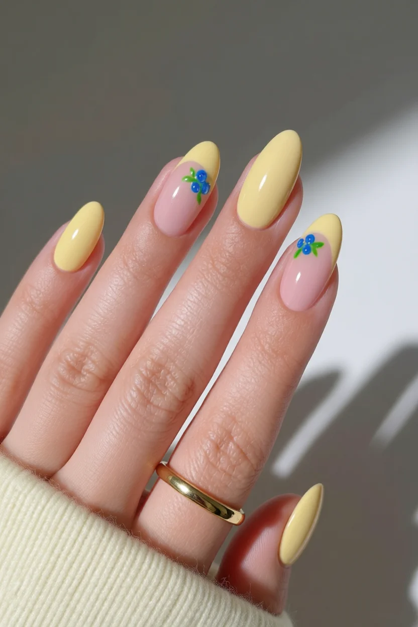 Uñas almendradas en amarillo pastel y rosa con pequeña decoración de flores azules