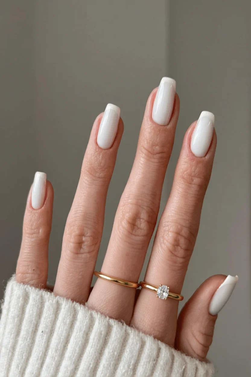 Mano con uñas largas en forma de almendra color blanco lechoso y anillos dorados