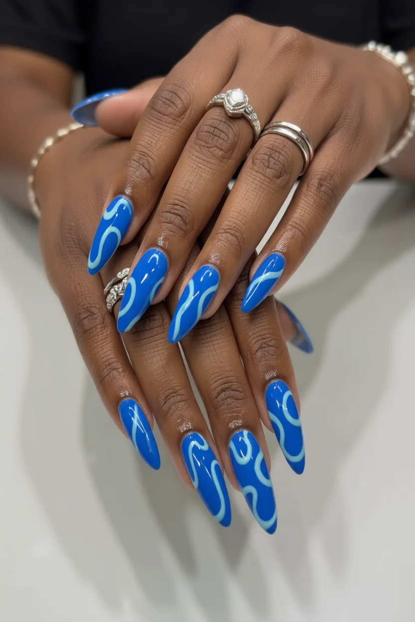 Uñas largas almendradas con base azul eléctrico y ondas decorativas en tono claro