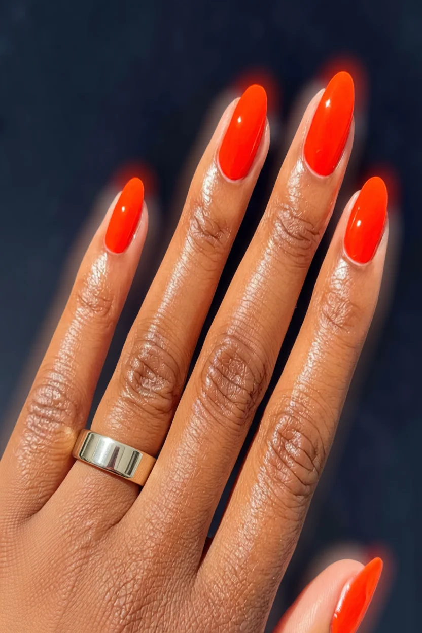 Mano con uñas ovaladas esmaltadas en naranja brillante y anillo de plata