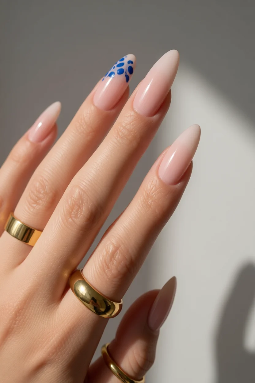 Mano con uñas largas en forma de almendra color nude y diseño francés con lunares azules