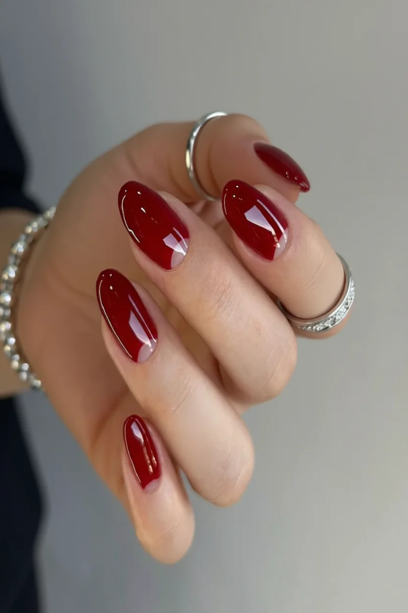 Mano con uñas ovaladas esmaltadas en rojo burdeos brillante con delicado efecto French en las puntas