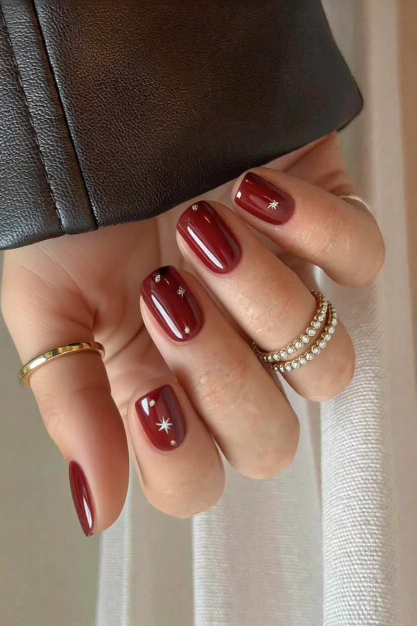 Uñas ovaladas en rojo vino con diseño de estrellas plateadas