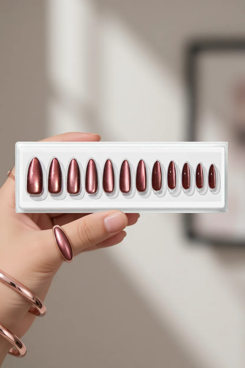 Set de uñas press-on forma almendra con acabado metálico degradado en tonos cobre rosa sostenidas en mano
