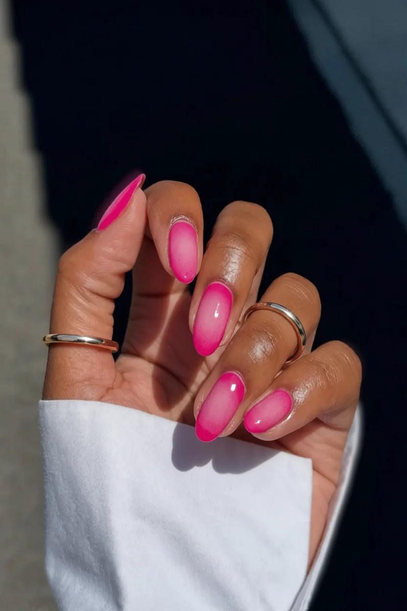 Mano con uñas almendradas rosa fucsia en degradado brillante