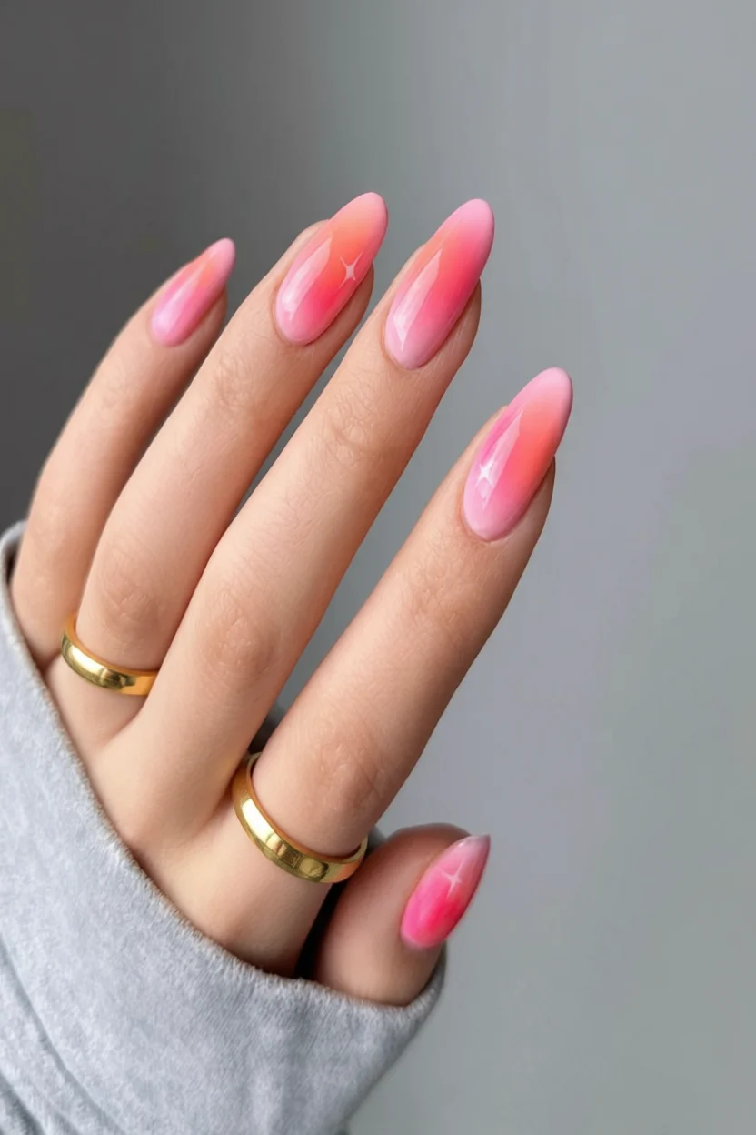 Uñas largas ovaladas con diseño degradado rosa y pequeñas estrellas brillantes