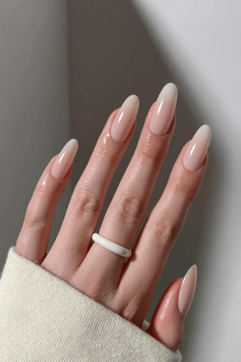 Mano con uñas largas almendradas en degradado nude a blanco con acabado brillante