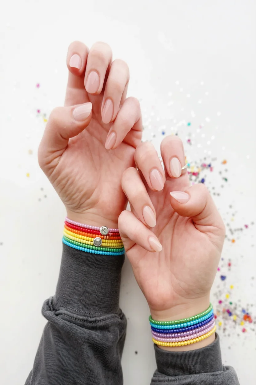Manos con uñas nude naturales y pulseras multicolores de cuentas arcoíris