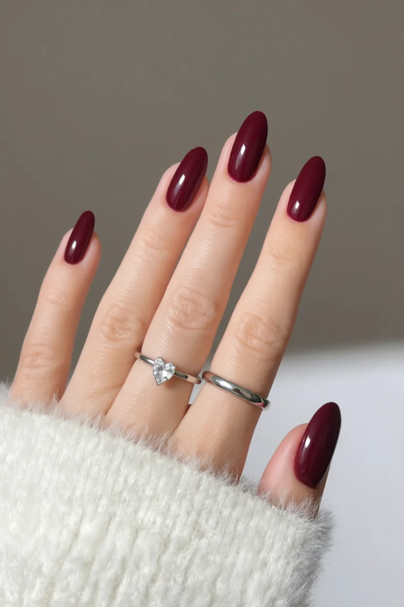 Mano con uñas ovaladas esmaltadas en rojo vino oscuro brillante