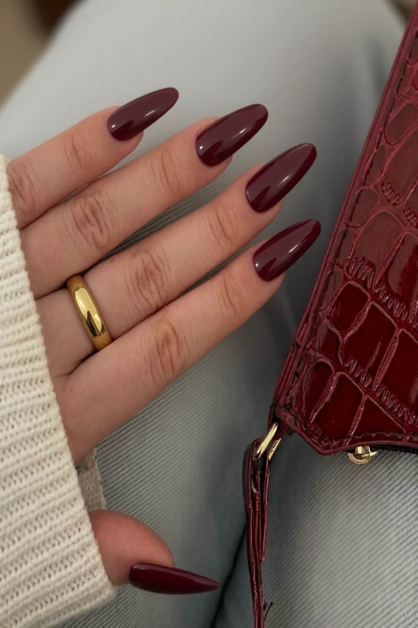 Uñas largas estilo almendra con esmalte borgoña brillante y anillo dorado