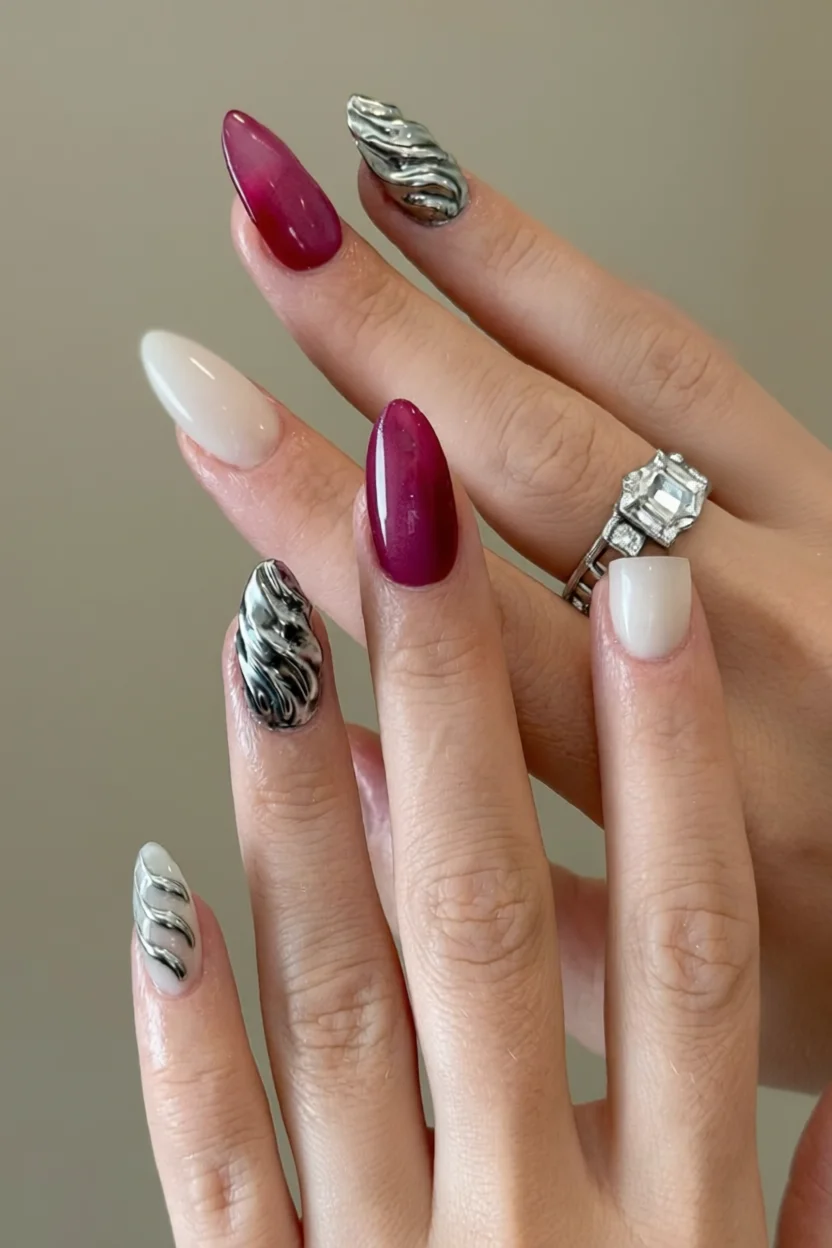 Mano con uñas largas en forma de almendra, una combinación de esmalte berry intenso, base nude clara y acentos en plata con efecto metalizado retorcido