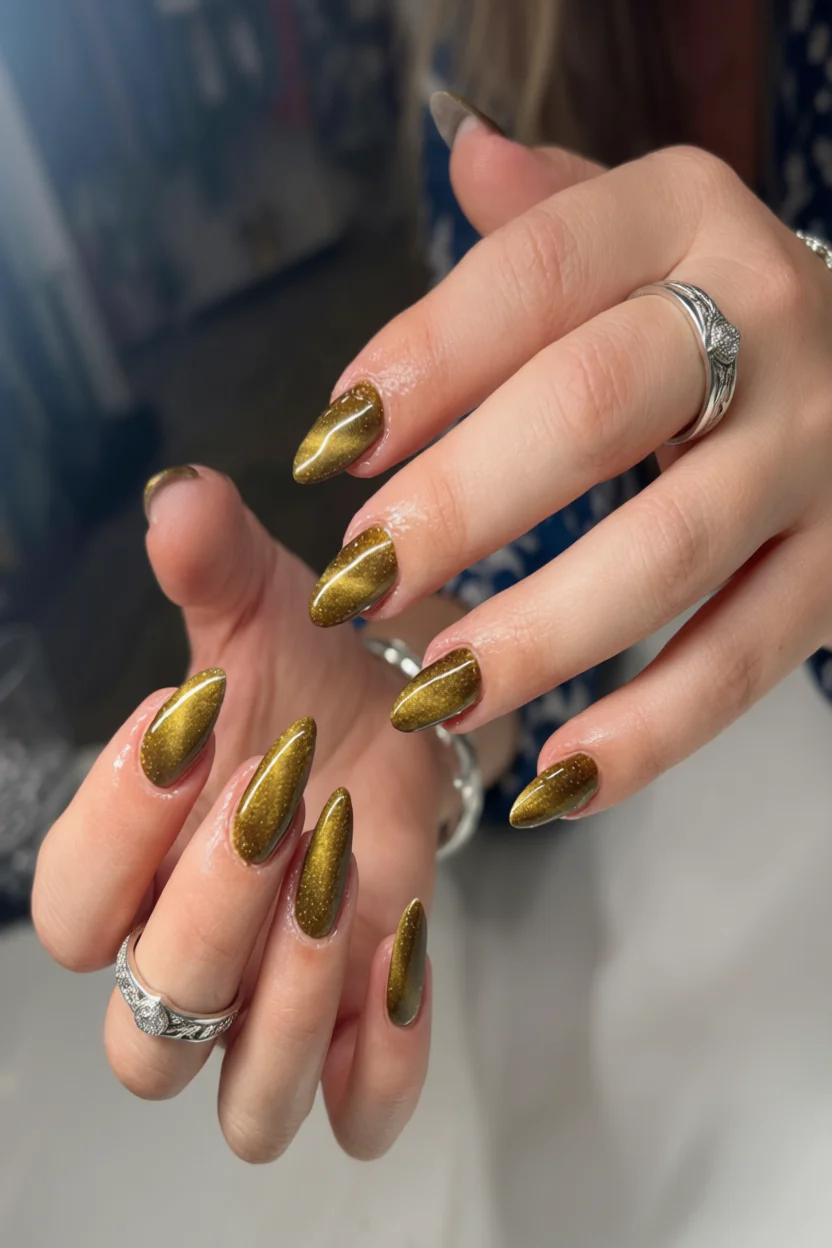 Uñas largas almendradas con esmalte dorado metálico brillante con partículas de brillo
